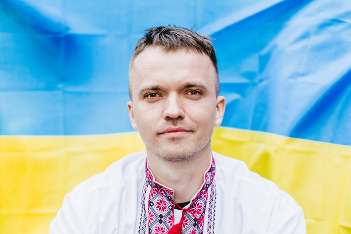 Maksym Zubkov standing before the Ukrainian flag